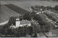 Flygfoto av Ostads kyrka. Odaterat. Forlag David Carlsson, Sjovik. A B Almquist Coster, Halsingborg. Foto Lilljqvist